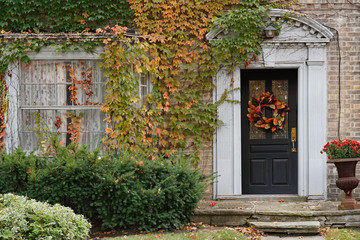 Front door of old brick house with fall wreath and surrounded by ivy