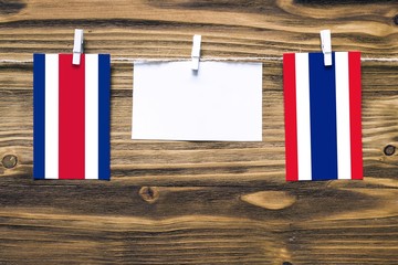 Hanging flags of Costa Rica and Thailand attached to rope with clothes pins with copy space on white note paper on wooden background.Diplomatic relations between countries.