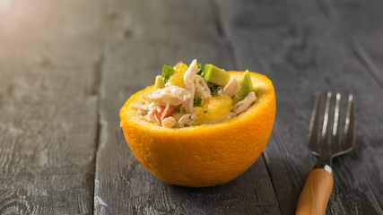 A fork with a wooden handle and half an orange with a salad on a wooden table.