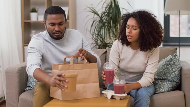 eating and people concept - happy african american couple with takeaway food and smoothie drinks at home