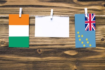 Hanging flags of Cote D'Ivoire and Tuvalu attached to rope with clothes pins with copy space on white note paper on wooden background.Diplomatic relations between countries.