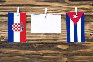 Hanging flags of Croatia and Cuba attached to rope with clothes pins with copy space on white note paper on wooden background.Diplomatic relations between countries.