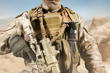 Soldier in uniform standing with rifle in desert.