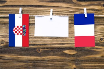 Hanging flags of Croatia and France attached to rope with clothes pins with copy space on white note paper on wooden background.Diplomatic relations between countries.