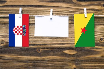 Hanging flags of Croatia and French Guiana attached to rope with clothes pins with copy space on white note paper on wooden background.Diplomatic relations between countries.