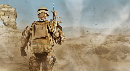 Soldier in uniform standing fully equipped rear view in desert.