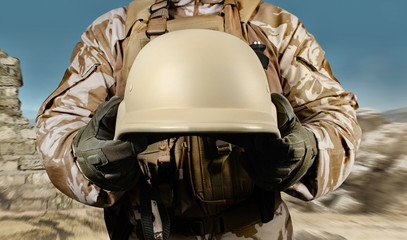 Soldier in uniform holding armor helmet in desert.