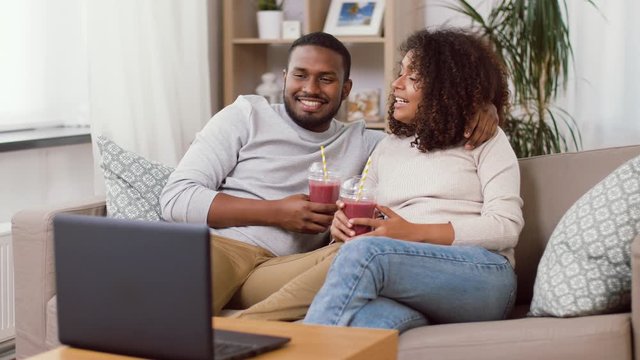 eating and people concept - happy african american couple with laptop and takeaway smoothie drinks at home
