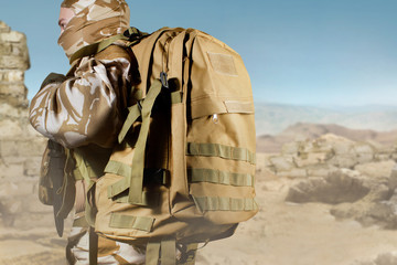 Soldier in uniform standing with backpack on desert background.