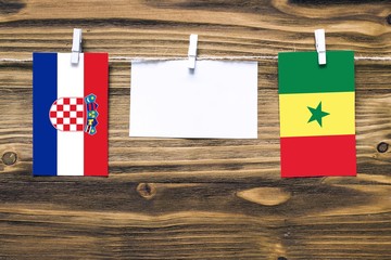 Hanging flags of Croatia and Senegal attached to rope with clothes pins with copy space on white note paper on wooden background.Diplomatic relations between countries.