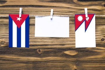 Hanging flags of Cuba and Nepal attached to rope with clothes pins with copy space on white note paper on wooden background.Diplomatic relations between countries.