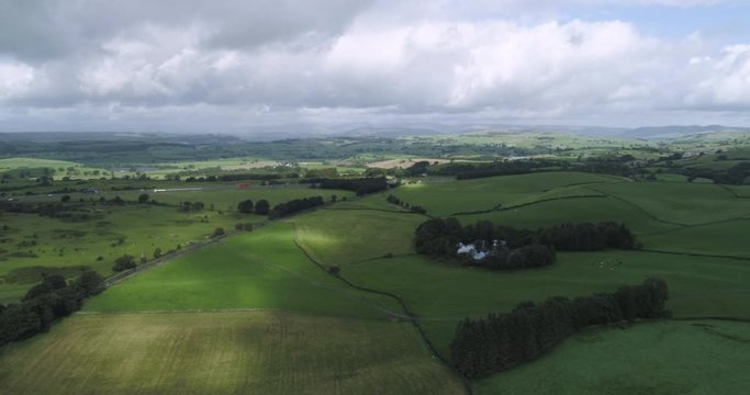Aerial 4K Slow motion shot of Sedbergh in Lake District. Flyover fields and countryside with view of busy road in background, cloudy day.