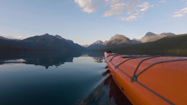 Kayaking in Lake McDonald during a sunny summer sunset with American Rocky Mountains in the background. Taken in Glacier National Park, Montana, USA.