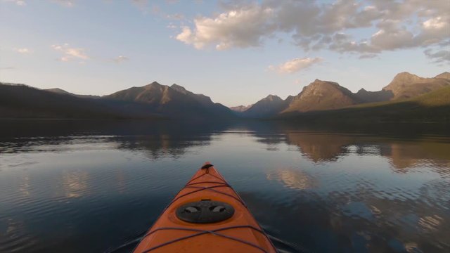 Kayaking in Lake McDonald during a sunny summer sunset with American Rocky Mountains in the background. Taken in Glacier National Park, Montana, USA.