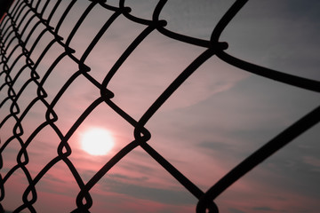 autumn sunrise shining through the metal chain link fence background texture
