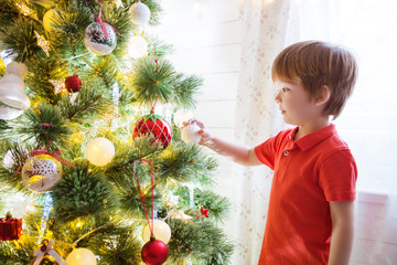 Xmas party celebration. Little boy decorating Christmas tree with toy balls