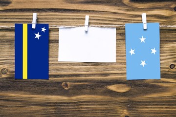 Hanging flags of Curacao and Micronesia attached to rope with clothes pins with copy space on white...