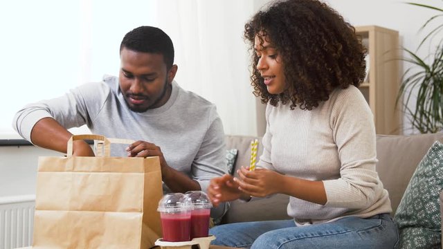 eating and people concept - happy african american couple with takeaway food and smoothie drinks at home