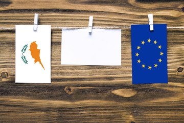 Hanging flags of Cyprus and European Union attached to rope with clothes pins with copy space on white note paper on wooden background.Diplomatic relations between countries.