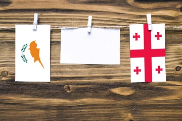 Hanging flags of Cyprus and Georgia attached to rope with clothes pins with copy space on white note paper on wooden background.Diplomatic relations between countries.