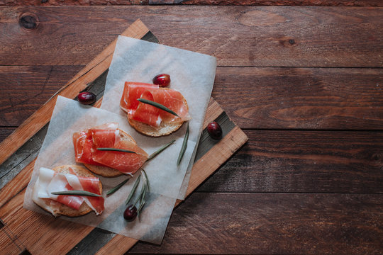 Prosciutto with bread, olives on backing paper. Cured meat served on wooden board with bread. Top view copy space for text.