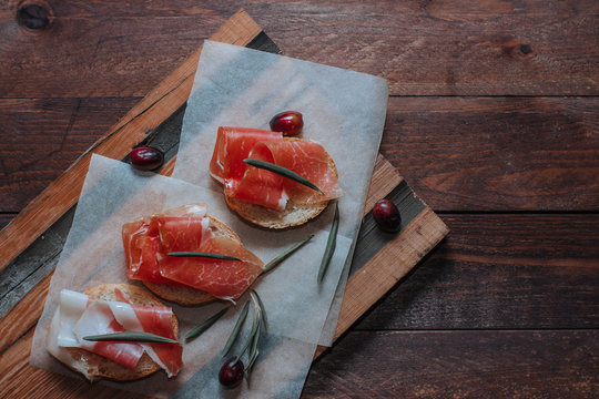 Prosciutto with bread and olives on backing paper. Cured meat served on wooden board. Top view
