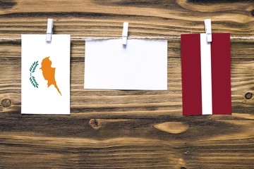 Hanging flags of Cyprus and Latvia attached to rope with clothes pins with copy space on white note paper on wooden background.Diplomatic relations between countries.