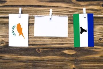 Hanging flags of Cyprus and Lesotho attached to rope with clothes pins with copy space on white...