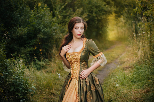 Portrait of an attractive, young girl in a green rococo dress strolling through a park. Model with clean skin.