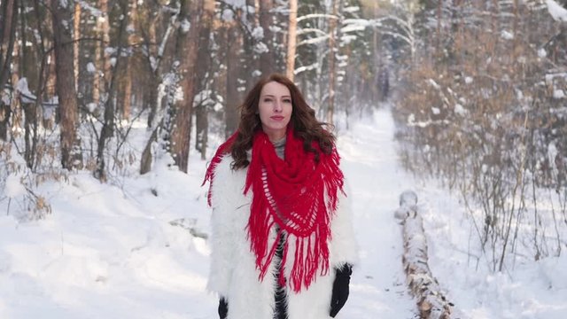 Attractive blonde in a white fur coat and red scarf posing on the background of a winter forest. Model in a white fur coat on a snowy background