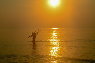 Net Fisherman ocean wading with tropical sunrise seascape , Thailand.