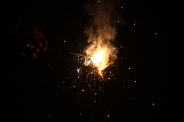 Fototapeta na wymiar human Hand holding the sparkler on sparkling with dark background with some white smoke on the deepavali / dewali celebration