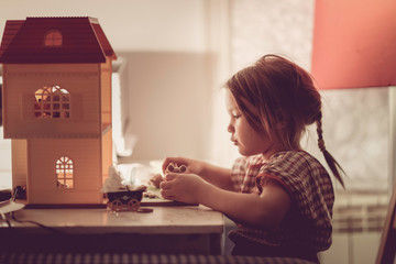 Girl child with pigtail plays with dollhouse