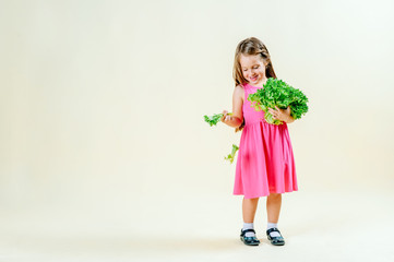 healthy eating concept, little girl in a pink dress on a light plain background holds lettuce