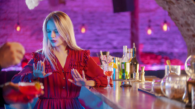 Gorgeous blonde young woman sitting by the bartender stand and cheking out her manicure nails