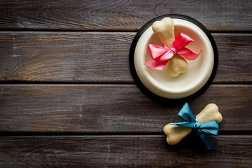Dog's birthday concept. Chewing bones with bow in bowl on dark wooden background top view space for text