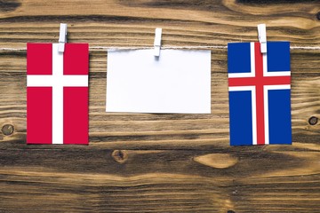 Hanging flags of Denmark and Iceland attached to rope with clothes pins with copy space on white note paper on wooden background.Diplomatic relations between countries.