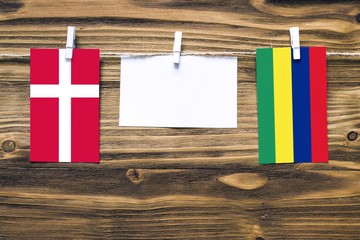 Hanging flags of Denmark and Mauritius attached to rope with clothes pins with copy space on white note paper on wooden background.Diplomatic relations between countries.