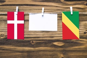 Hanging flags of Denmark and Republic Of The Congo attached to rope with clothes pins with copy space on white note paper on wooden background.Diplomatic relations between countries.