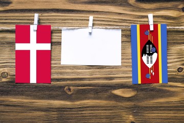 Hanging flags of Denmark and Swaziland attached to rope with clothes pins with copy space on white note paper on wooden background.Diplomatic relations between countries.