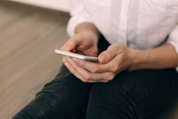 Woman hand holding white mobile phone and sitting on sofa at home.