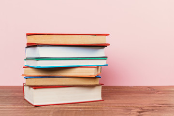 A simple composition of many hardback books, raw books on a wooden table and a pale pink background