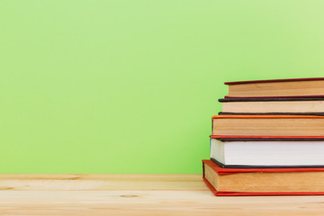 Simple composition of many hardback books, raw of books on wooden table and light green background