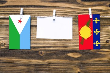 Hanging flags of Djibouti and Guadeloupe attached to rope with clothes pins with copy space on...