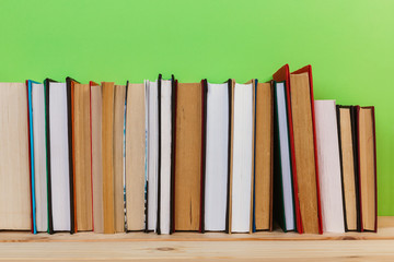 Simple composition of many hardback books, raw of books on wooden table and light green background