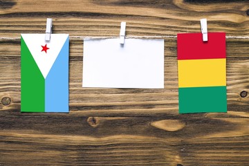 Hanging flags of Djibouti and Guinea attached to rope with clothes pins with copy space on white note paper on wooden background.Diplomatic relations between countries.