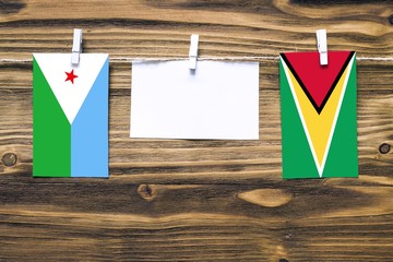Hanging flags of Djibouti and Guyana attached to rope with clothes pins with copy space on white...