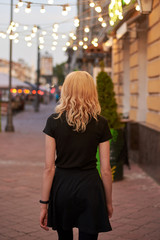 Fototapeta premium A beautiful young girl walks along a city street and looks at the garlands, back view.