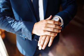 Men's wrist watch, the man is watching the time. Businessman clock, businessman checking time on his wristwatch. Groom's hands in a suit adjusting wristwatch, wedding preparations, groom accessories.