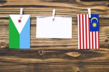 Hanging flags of Djibouti and Malaysia attached to rope with clothes pins with copy space on white...
